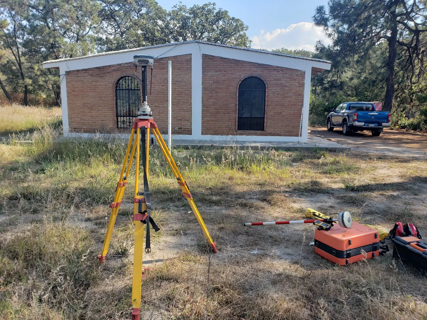 Tripié con receptor GNSS frente a una casa de ladrillo durante una medición de construcción